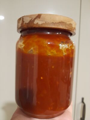 A jar of homemade Dragon Sauce with a wooden lid, filled with thick red sauce showing a glossy surface and a few visible chilli flakes.