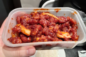 A close-up of crispy fried chicken pieces covered in a thick, glossy red-brown Dragon Sauce with visible onion slices.